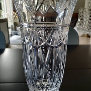 Peut inclure: Un vase en verre transparent avec un motif en cristal taillé. Le vase a une large ouverture et une base étroite.