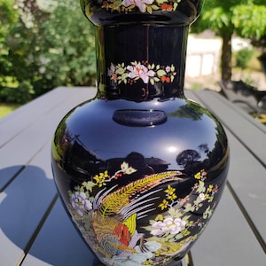 Puede incluir: Un jarrón de cerámica negro con un diseño floral y de pájaros en oro y multicolor.