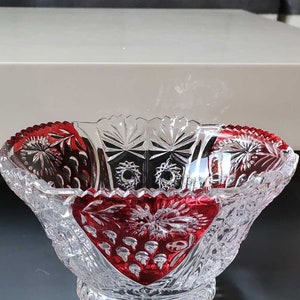 Può includere: Una ciotola di vetro trasparente con un design in vetro tagliato e un bordo rosso. La ciotola è su una superficie grigia.