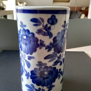 Pode incluir: Um vaso de cerâmica branca com um padrão floral azul. O vaso tem forma cilíndrica e um design simples.