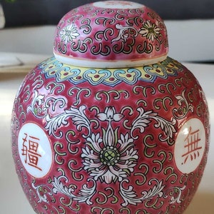 Op de afbeelding: Een rode en witte porseleinen pot met een deksel, versierd met bloem- en rolpatronen. De pot heeft twee Chinese karakters aan de zijkanten, "福" en "無".