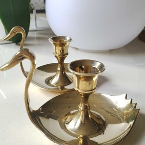 May include: A pair of gold swan-shaped candle holders with two candle cups. The candle holders are made of brass and have a polished finish.