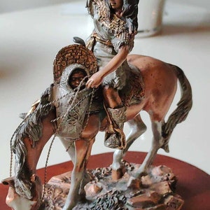 May include: A bronze sculpture of a Native American woman riding a horse with a child wrapped in a blanket on the horse's back. The sculpture is on a wooden base with the words "Short Rest" inscribed on it.