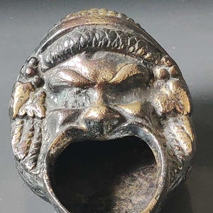 May include: A small, bronze, decorative ashtray shaped like a face with a wide open mouth. The face has a crown and a detailed design.