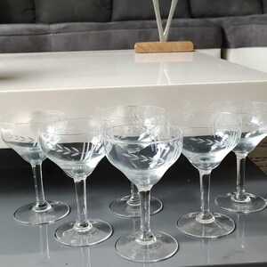 May include: Six clear glass stemmed drinking glasses with etched floral designs on a white surface.