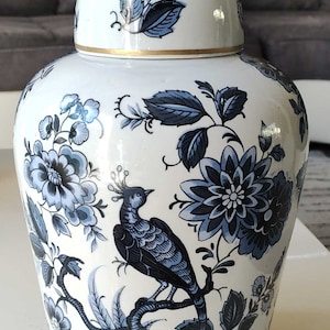 Könnte beinhalten: Eine weiße Porzellanvase mit einem blauen und weißen Blumendesign. Die Vase zeigt einen Vogel, der auf einem Ast mit Blättern und Blumen sitzt. Der Deckel hat einen goldenen Rand.
