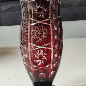 Puede incluir: Un jarrón de cristal rojo con intrincados diseños de vidrio cortado. El jarrón tiene una boca ancha y una base redonda.