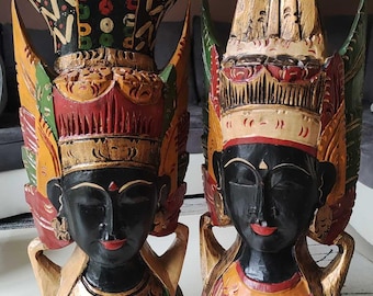 May include: Two wooden sculptures of people with ornate headdresses and colourful clothing. The sculptures are painted in shades of red, green, gold, and black.