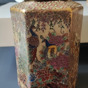 Op de afbeelding: Een zeshoekige keramische gemberpot met bijpassend deksel, voorzien van een gedetailleerd veelkleurig ontwerp van pauwen en bloemmotieven op een crèmekleurige craquelé glazuurachtergrond, geaccentueerd met goudkleurige randen.
