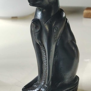 May include: Black Egyptian cat statue with hieroglyphics on the base and a cobra on the chest.