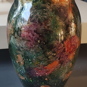 Può includere: Un vaso decorativo in vetro dal design unico e colorato. Il vaso presenta una miscela di tonalità verdi, viola e arancioni, creando un effetto marmorizzato. Il vaso ha un corpo ampio e un bordo leggermente svasato, adatto per composizioni floreali.