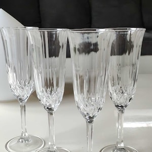 May include: Four clear glass champagne flutes with a diamond pattern. The flutes are arranged in a row on a white surface.