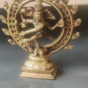 Peut inclure: Une statue en laiton d'une divinité dansante, probablement Shiva, avec des détails complexes. La figure est entourée d'un halo circulaire avec des extensions en forme de feuilles. La statue est montée sur une base carrée, mettant en valeur l'artisanat traditionnel.
