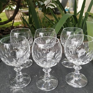Peut inclure: Six gobelets en verre transparent avec un motif en verre taillé. Les gobelets sont disposés en demi-cercle sur une surface gris foncé.