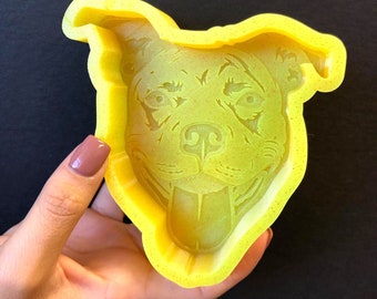 May include: A yellow silicone mold shaped like a dog's head. The mold has a detailed design of a dog's face with a tongue sticking out.