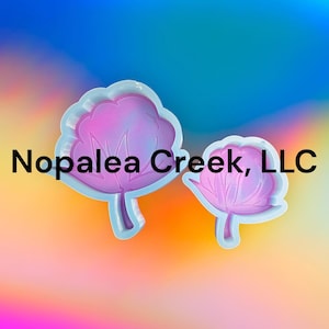 May include: Two silicone molds for making resin crafts. The molds are shaped like cotton flowers. The larger mold is light blue and the smaller mold is a darker blue. The molds are on a colorful background.