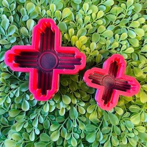 May include: Two red silicone molds shaped like the symbol of the Zia Pueblo, a Native American tribe in New Mexico. The symbol is a stylized sun with four rays.