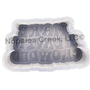 May include: A white silicone mold with the words "CROWD SURF" and "I AM" in a black, glittery font.