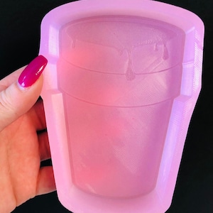 May include: A pink silicone mold shaped like a plastic cup with a textured surface and a dripping design.