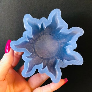 May include: A blue silicone mold shaped like the sun with a detailed design. The mold is designed for crafting and creating resin art.
