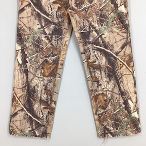 K&ouml;nnte beinhalten: Tarnhose in Braun-, Beige- und Gr&uuml;nt&ouml;nen. Das Design zeigt ein realistisches Waldmuster mit &Auml;sten und Bl&auml;ttern. Die unteren S&auml;ume sind ausgefranst. Die Hose besteht aus einem strapazierf&auml;higen Stoff.