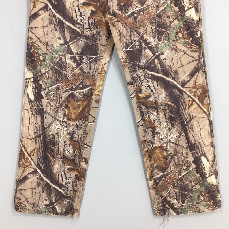 K&ouml;nnte beinhalten: Tarnhose in Braun-, Beige- und Gr&uuml;nt&ouml;nen. Das Design zeigt ein realistisches Waldmuster mit &Auml;sten und Bl&auml;ttern. Die unteren S&auml;ume sind ausgefranst. Die Hose besteht aus einem strapazierf&auml;higen Stoff.