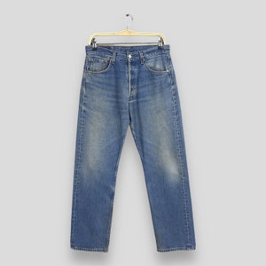 May include: Blue denim jeans hanging on a gold-colored hanger. The jeans have a classic five-pocket design, a button fly, and a faded wash. The jeans are straight-legged and appear to be a vintage style.