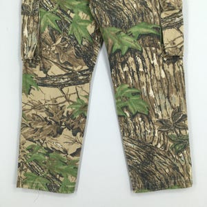 Puede incluir: Pantalones cargo de camuflaje con un patr&oacute;n forestal realista en tonos marr&oacute;n, verde y beige. Los pantalones tienen un dise&ntilde;o cargo cl&aacute;sico con bolsillos y una pernera recta. La tela parece duradera y adecuada para actividades al aire libre.