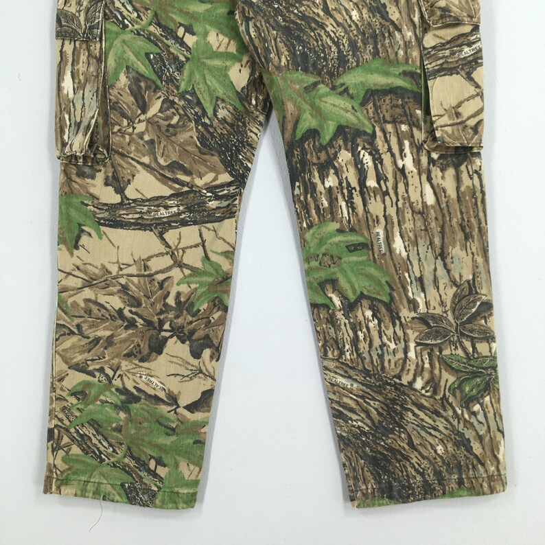 Puede incluir: Pantalones cargo de camuflaje con un patr&oacute;n forestal realista en tonos marr&oacute;n, verde y beige. Los pantalones tienen un dise&ntilde;o cargo cl&aacute;sico con bolsillos y una pernera recta. La tela parece duradera y adecuada para actividades al aire libre.