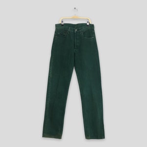 Op de afbeelding: Een donkergroene spijkerbroek die aan een houten hanger hangt. De broek heeft een klassieke vijf-zak stijl en een knoopsluiting.