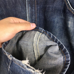 Puede incluir: Primer plano de unos vaqueros de mezclilla azules, que muestran la textura de la tela y los detalles de las costuras. El dobladillo est&aacute; doblado, revelando el interior de la mezclilla. Los vaqueros tienen un aspecto cl&aacute;sico y desgastado.