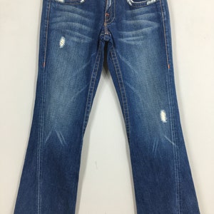 May include: Blue denim jeans with a bootcut leg. The jeans have a distressed look with faded areas and small rips. Orange stitching accents the pockets and seams. The back pockets have a decorative design.