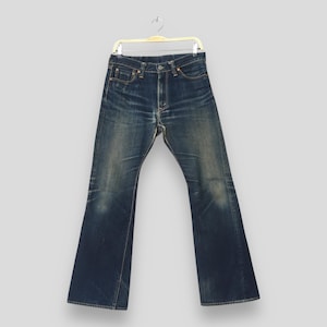May include: A pair of dark blue denim jeans featuring a faded wash, whiskering at the hips, and a classic five-pocket design. The jeans are suspended from a white plastic hanger and display a straight-leg cut with visible stitching details.