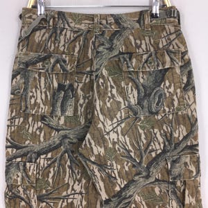 Pu&ograve; includere: Pantaloni cargo mimetici con un motivo realistico di corteccia d'albero nei toni del marrone, verde e beige. I pantaloni hanno pi&ugrave; tasche e una chiusura con bottoni. Il tessuto sembra essere un materiale resistente, adatto alle attivit&agrave; all'aperto.