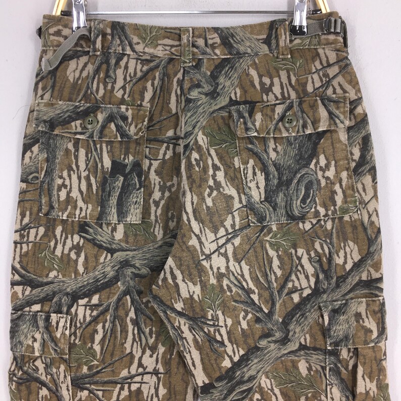 Pu&ograve; includere: Pantaloni cargo mimetici con un motivo realistico di corteccia d'albero nei toni del marrone, verde e beige. I pantaloni hanno pi&ugrave; tasche e una chiusura con bottoni. Il tessuto sembra essere un materiale resistente, adatto alle attivit&agrave; all'aperto.
