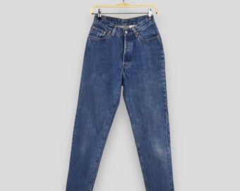 May include: Blue denim jeans hanging on a wooden hanger. The jeans have a button fly, classic five-pocket design, and a faded wash. The jeans are a vintage style.