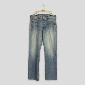 Puede incluir: Vaqueros de mezclilla azul claro con bragueta de botones, exhibidos en una percha. Los vaqueros tienen un lavado descolorido y un diseño clásico de cinco bolsillos. Los vaqueros son de estilo recto.