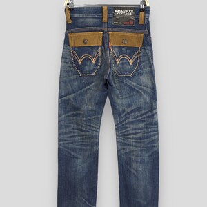 May include: Vintage blue denim jeans with brown suede-like back pockets and detailing. The jeans have a faded wash and a red tag. The back pockets feature a unique stitch design. The label reads "EXCLUSIVE VINTAGE".