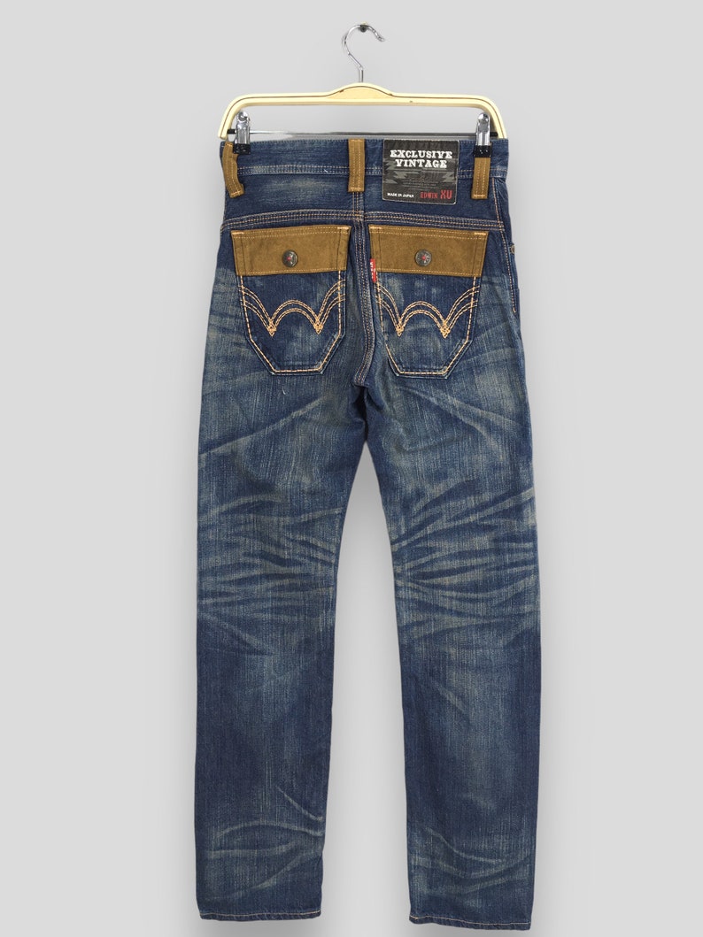 May include: Vintage blue denim jeans with brown suede-like back pockets and detailing. The jeans have a faded wash and a red tag. The back pockets feature a unique stitch design. The label reads "EXCLUSIVE VINTAGE".