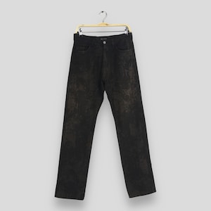 May include: Black denim jeans with a unique, textured pattern. The jeans are straight-legged and feature classic five-pocket styling. They are displayed on a gold-colored hanger against a neutral background. The jeans have a button and zipper closure.