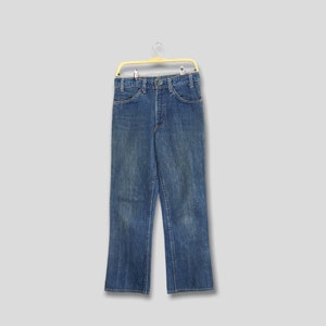 May include: Blue denim jeans with a button closure and pockets, hanging on a yellow hanger. The jeans have a classic, straight-leg fit and show signs of wear.