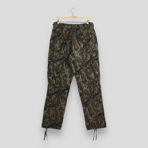 Pu&ograve; includere: Pantaloni cargo mimetici con un motivo boschivo nei toni del marrone, verde e grigio. I pantaloni sono appesi a una gruccia dorata. Hanno pi&ugrave; tasche e coulisse alle caviglie.