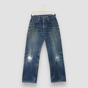 May include: Blue denim jeans with a high waist and a relaxed fit, hanging on a gold hanger. The jeans have distressed details, including rips on the knees. The denim has a faded appearance.