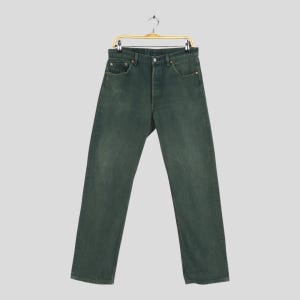 Op de afbeelding: Donkergroene spijkerbroek aan een goudkleurige hanger. De jeans heeft een knoopsluiting, een klassiek ontwerp met vijf zakken en een licht vervaagde uitstraling. De broek heeft rechte pijpen en lijkt een vintage stijl te hebben.