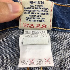 May include: Close-up of a denim garment tag with text: "RN#112790 100% COTTON MACHINE WASH COLD. TUMBLE DRY MEDIUM. COLOR MAY TRANSFER WHEN NEW. WASH INSIDE OUT TO RETAIN COLOR." and "CUT#300072 STYLE#04-603 100% COTTON."