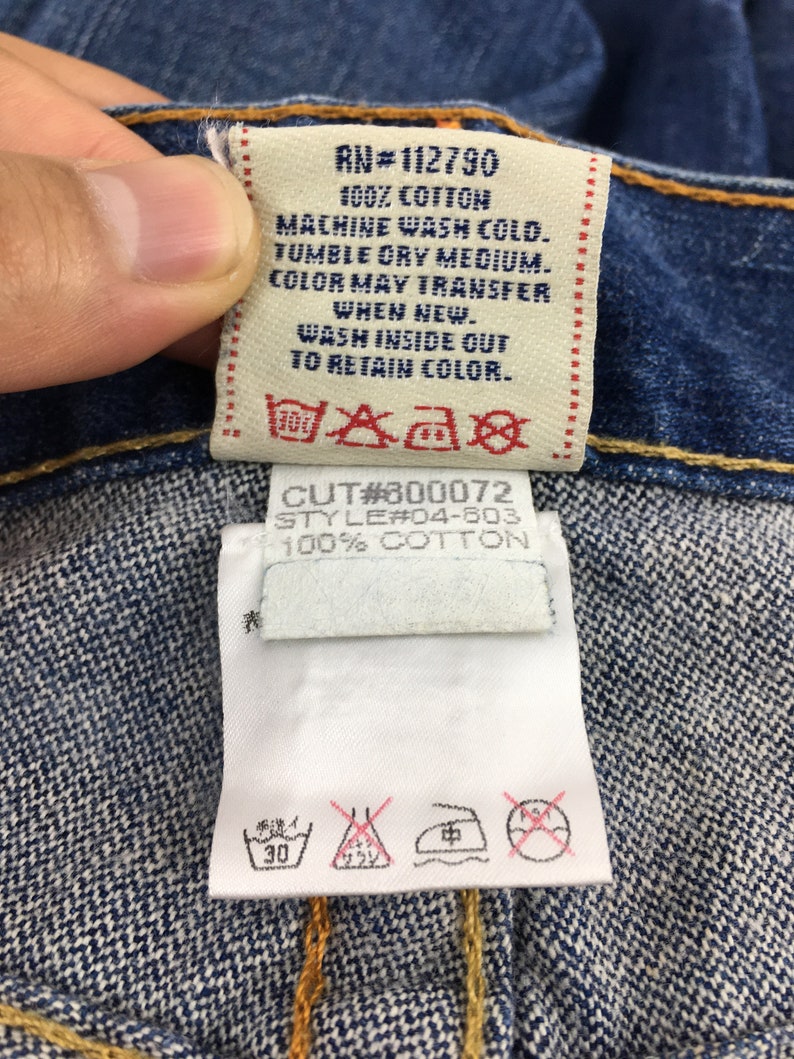 May include: Close-up of a denim garment tag with text: "RN#112790 100% COTTON MACHINE WASH COLD. TUMBLE DRY MEDIUM. COLOR MAY TRANSFER WHEN NEW. WASH INSIDE OUT TO RETAIN COLOR." and "CUT#300072 STYLE#04-603 100% COTTON."