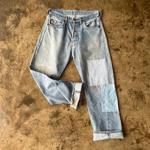 Puede incluir: Vaqueros de mezclilla azul claro con parches en la pierna derecha. Los vaqueros tienen bragueta con botones, diseño clásico de cinco bolsillos y dobladillos con vuelta. La mezclilla tiene un aspecto descolorido y desgastado.