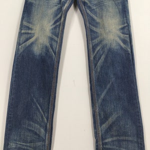 May include: Blue denim jeans with a faded wash and contrasting stitching. The jeans have a classic five-pocket design and a straight leg fit. The denim has a worn appearance with lighter areas on the thighs and knees.