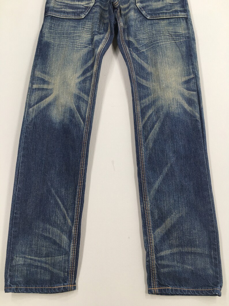 May include: Blue denim jeans with a faded wash and contrasting stitching. The jeans have a classic five-pocket design and a straight leg fit. The denim has a worn appearance with lighter areas on the thighs and knees.