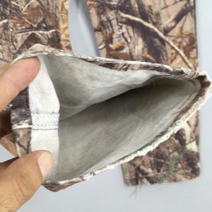 K&ouml;nnte beinhalten: Nahaufnahme eines Camouflage-Hosenbeins, das das Innenfutter zeigt. Die Hose hat ein realistisches Baumrindenmuster in Braun-, Beige- und Gr&uuml;nt&ouml;nen. Das Innenfutter ist ein hellgrauer Stoff. Der Saum ist umgeschlagen und zeigt die Innennaht.